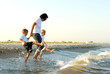 woman holding hands of two young boys, as they splash in water