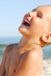 Close up portrait of young boy laughing with delight by sea.