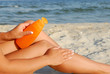 Woman applying lotion to leg on sandy beach by water. Woman applying lotion to leg on sandy beach by water.