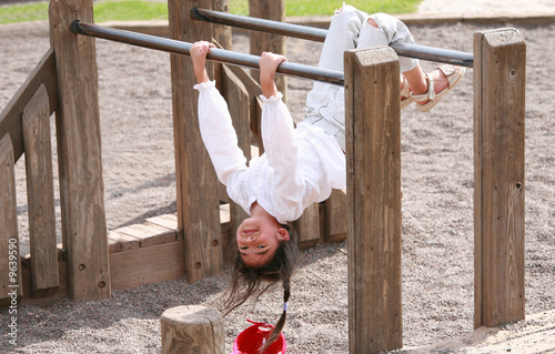 Photo: Little girl hanging upside down on parallel bars at playground Little girl hanging upside down on parallel bars at playground