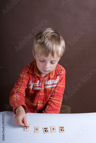 Photo: The little boy displays on a table of a card with figures The little boy displays on a table of a card with figures