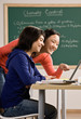 Student with laptop doing homework with friend in classroom