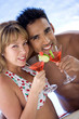 Happy young couple relaxing by the pool enjoying cocktails