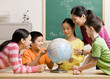 Teacher and students viewing globe in geography classroom