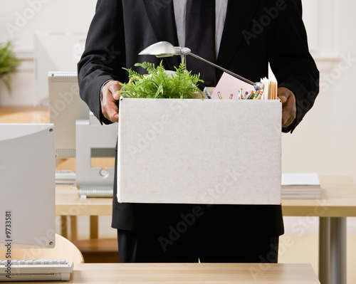Photo: Fired businessman packing personal desk items in box Fired businessman packing personal desk items in box