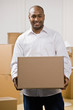 Happy man moving into new home carrying cardboard box