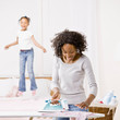 Housewife ironing laundry while girl jumps on bed