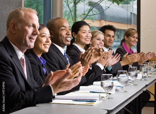 Photo: Multi-ethnic co-workers sitting in a row, applauding at table Multi-ethnic co-workers sitting in a row, applauding at table