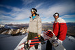 Two snowboarders stand on a peak over looking a spectacular view
