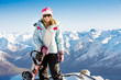 Woman holding snowboard with mountains in background