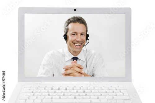 Photo: Mid adult businessman wearing headset on screen of laptop Mid adult businessman wearing headset on screen of laptop