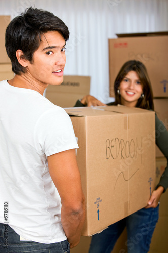 Foto: couple moving homes smiling and carrying a carton box couple moving homes smiling and carrying a carton box