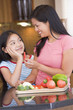 Mother Offering Daughter A Piece Of Freshly Chopped Pepper