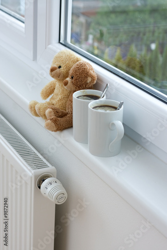Photo: Two teddy bears sitting on radiator in home. Two teddy bears sitting on radiator in home.
