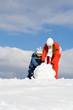 Mother with kid making snowman in winter park
