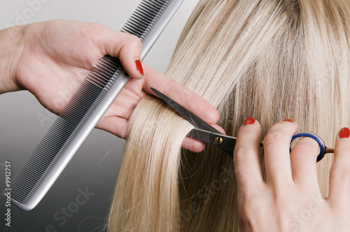 Photo: hairdresser cutting blonde hair. closeup over grey background hairdresser cutting blonde hair. closeup over grey background