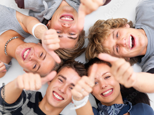 Photo: Happy young friends lying down showing thumbs up sign Happy young friends lying down showing thumbs up sign