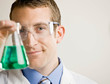 Scientist wearing safety goggles examining beaker of liquid