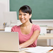 Happy student doing homework on laptop in school classroom