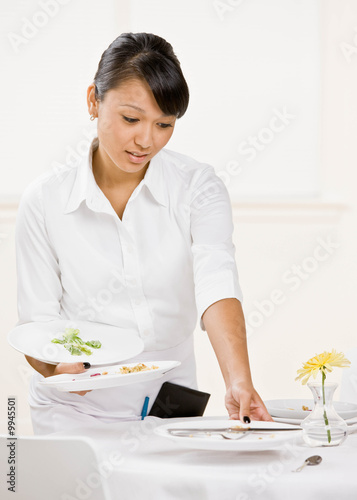 Photo: Waitress in restaurant clearing dirty dishes from table Waitress in restaurant clearing dirty dishes from table