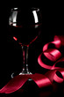 glass of red wine and red ribbon over black background
