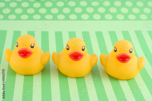Photo: three child's rubber duck on top of green striped background three child's rubber duck on top of green striped background