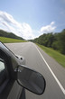 Vehicle, with large rear view mirror, speeds down a country road