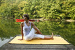 Woman doing yoga on lake in park in autumn
