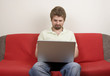 Casual man sitting on the sofa and works on the laptop