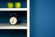 Photo: Green apple and clock inside white bookcase in blue room Green apple and clock inside white bookcase in blue room
