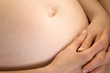 Pregnant woman naked belly with navel and hands around