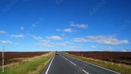 Photo: Red car travels on Yorkshire moors country road Red car travels on Yorkshire moors country road