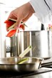 Chef hands add vegetables on a frying pan on pro-kitchen