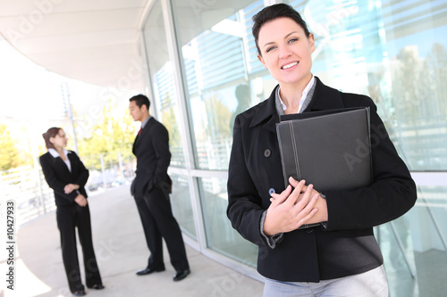 A pretty business woman at office with team in background A pretty business woman at office with team in background