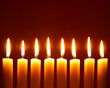 Eight alight candles close-up over red background