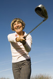 Photo: Germany, Bavaria, Ammersee, Senior woman swinging golf club, smiling, low angle view Germany, Bavaria, Ammersee, Senior woman swinging golf club, smiling, low angle view