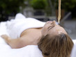 Young woman lying in spa with oil being poured on forehead, eyes closed