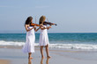 two young woman play violin on beach