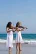 two young woman play violins on beach