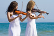 two young woman play violin on beach