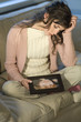Sad looking woman sitting cross-legged on a sofa looking at child's portrait