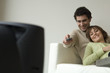 Smiling couple lying on a sofa, watching TV