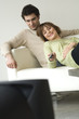 Smiling couple lying on a sofa, watching TV