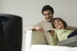 Smiling couple lying on a sofa, watching TV