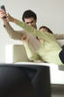 Couple lying on a sofa, watching TV, fighting over remote-control