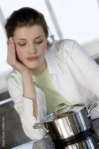 Photo: Young woman watching over saucepan on vitroceramic hob Young woman watching over saucepan on vitroceramic hob