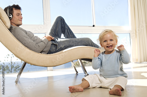 Photo: Father and little girl in living room, man listening to music, indoors Father and little girl in living room, man listening to music, indoors