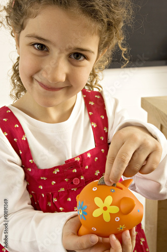 Photo: Girl putting a coin into a piggy bank Girl putting a coin into a piggy bank