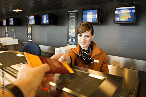 Photo: Female airline check-in attendant giving a passport and boarding pass to a passenger Female airline check-in attendant giving a passport and boarding pass to a passenger