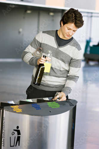 Photo: Mid adult man putting empty bottles into a garbage bin Mid adult man putting empty bottles into a garbage bin